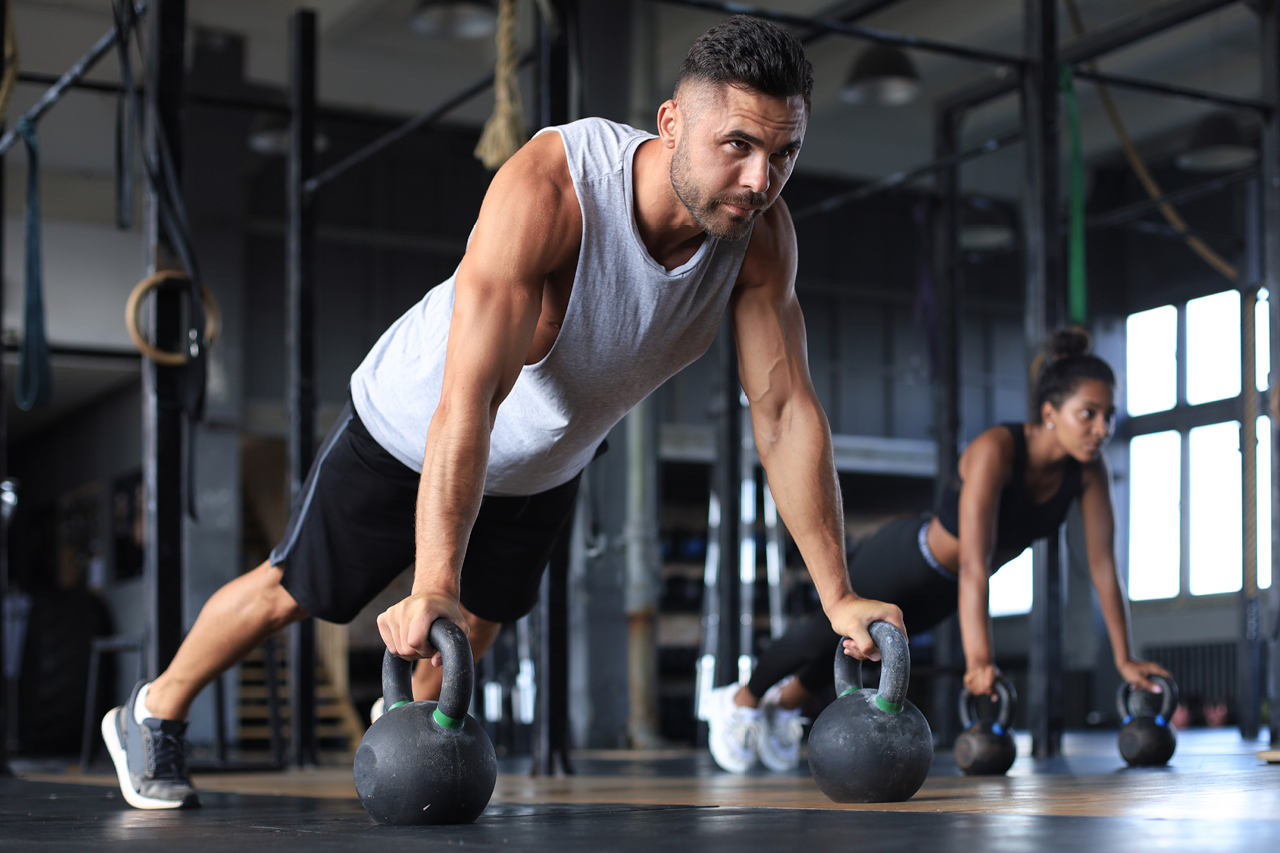 Fit man and woman perform functional fitness exercises in a gym setting