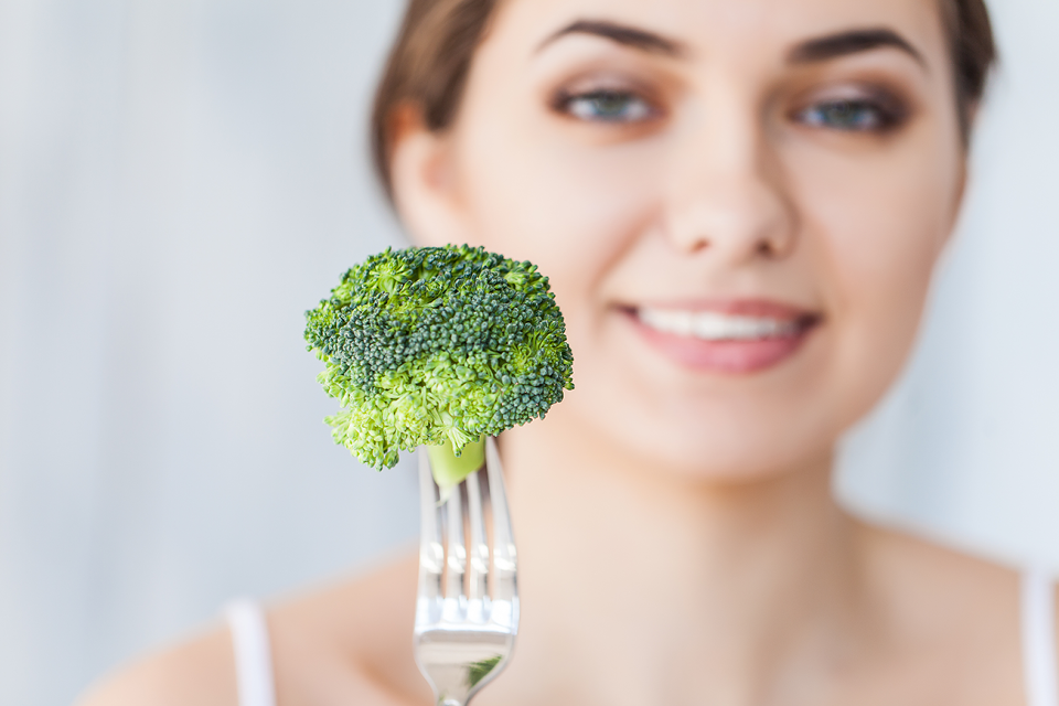Closeup of broccoli on a fork with smiling woman blurred in the background